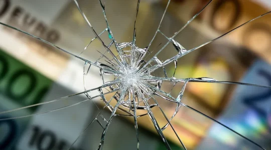 Vue macro d'un impact sur un pare-brise avec des billets d'euros flous en arrière-plan