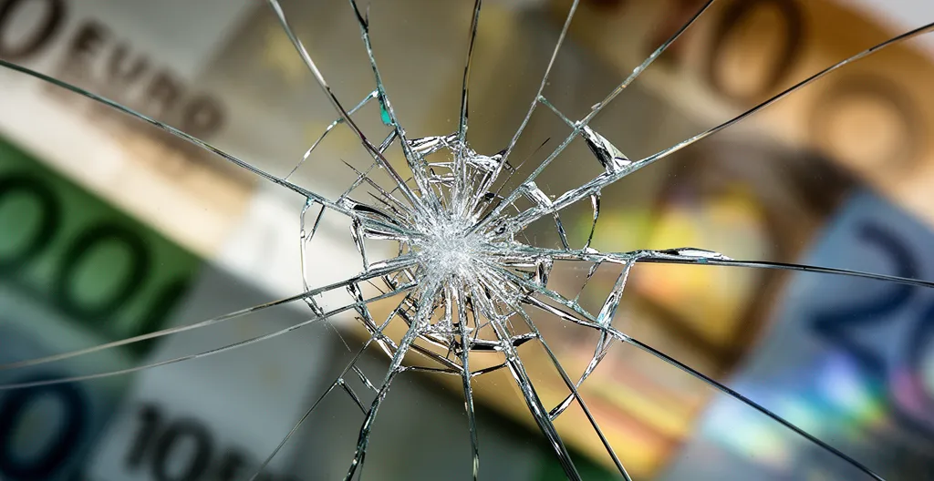 Vue macro d'un impact sur un pare-brise avec des billets d'euros flous en arrière-plan